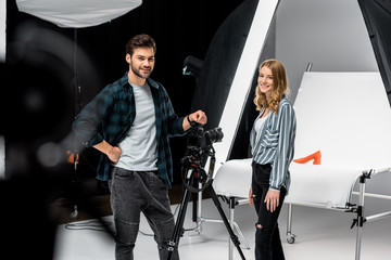 happy young photographers standing near professional photo equipment and smiling at camera in studio