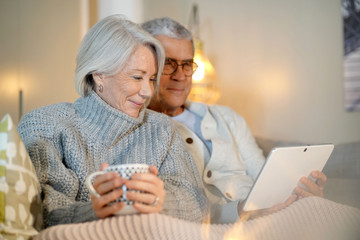  Senior couple relaxing at home on couch with tablet