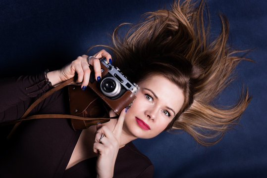 Portrait of beautiful woman lying down on a dark blue background and holding retro photo camera