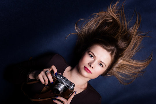 Portrait of beautiful woman lying down on a dark blue background and holding retro photo camera