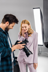 happy young photographer and model using photo camera together in studio