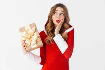 Portrait of optimistic woman 20s wearing Santa Claus red costume smiling and holding present box, isolated over white background