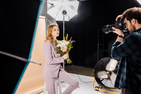 photographer shooting attractive young woman posing with flowers in photo studio