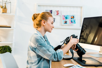 side view of smiling young female photographer working with camera in office - obrazy, fototapety, plakaty
