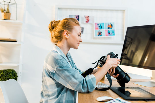 side view of smiling young female photographer working with camera in office