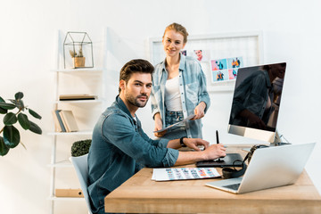 Obraz premium young photographers smiling at camera while retouching photos in office