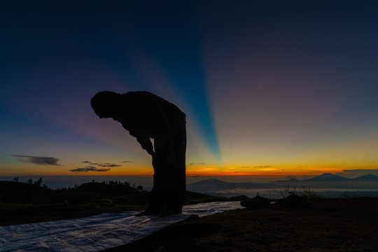 Unidentified man prays during sunrise on top of a mountain in Indonesia.