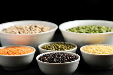 Set of different cereals and legumes in a white bowls on a black table