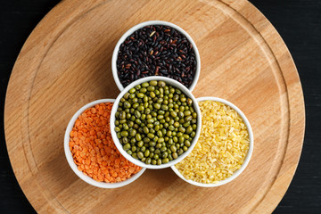 Set of different cereals and legumes in a white bowls on a black table, top view