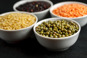 Set of different cereals and legumes in a white bowls on a black table