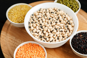 Set of different cereals and legumes in a white bowls on a black table