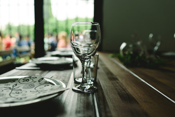 Wooden tables with cutlery plates and backlit glasses without anyone.