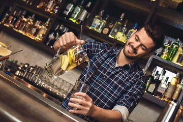 Young bartender standing at bar counter pouring vitamin water into glass happy