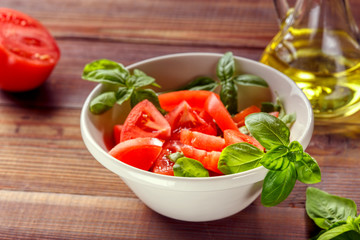 Fresh tomatoes with basil leaves in a ceramic bowl.