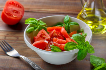Fresh tomatoes with basil leaves in a ceramic bowl.
