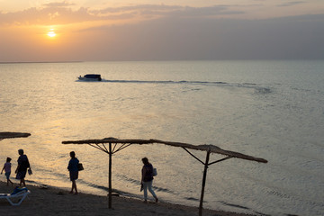 Sunset on the sea, people leave the beach in the evening and the boat sails from the shore of the Sea of Azov.