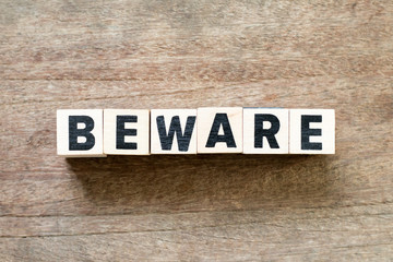 Letter block in word beware on wood background
