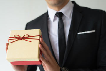 Close-up of businessman in suit presenting Christmas box. Unrecognizable man holding cute yellow box wrapped in thin ribbon. Christmas special offer concept