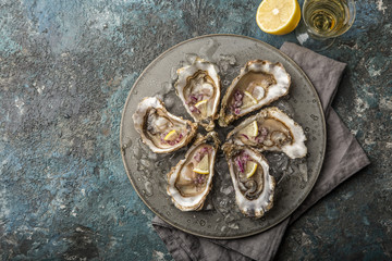 fresh raw oysters on gray plate served with lemon, red onion and wine vinegar