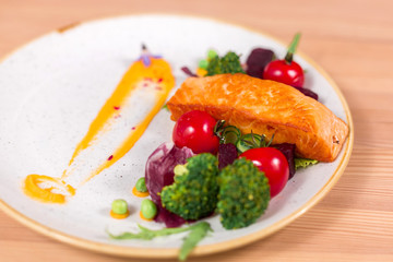 Fillet of salmon with vegetables, brocolli, cucumber, cherry and salad on white plate. Healthy food concept
