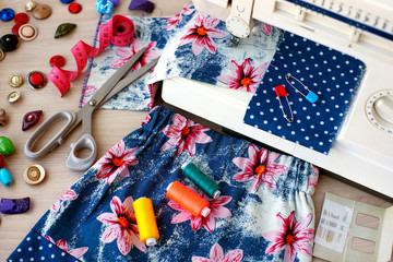 Fototapeta premium Sewing a skirt on a sewing machine. Sewing machine, fabric, children's skirt, tailoring scissors, measuring tape, threads and needles for sewing clothes.