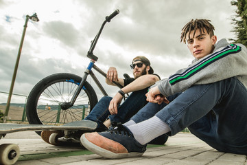 Obraz premium Young people riding bikes and skateboards in the city. Modern people with a skate and a bmx down the street.