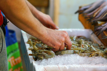 Detail of hands of fishmonger putting shrimps on display for sale in the central market of Athens