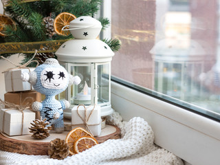 New Year and Christmas. Robots arrange a festive party. Toy tied in amigurami technique. Gifts - bracelets with charms. Christmas tree and lamp with a candle in the background.