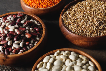 variety of beans in wooden bowls with oat groats on table