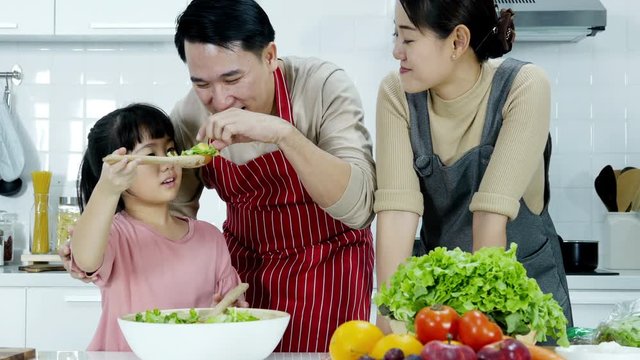 Father and mother teaching her daughter to cooking at kitchen. Little girl try to learn cooking skills from her father. People with healthcare, education and family concept.