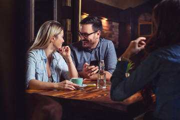 Fototapeta premium Handsome male holding a phone and looking at his girlfriend. Enjoying time in pub.
