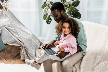 african american father and child using laptop while sitting on couch near wigwam © LIGHTFIELD STUDIOS