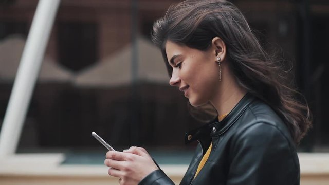 Young happy woman walking in the city street while using smartphone. Slow motion