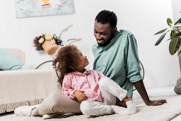 african american father and daughter comfortably sitting on floor