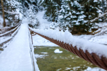 old suspension bridge across river, winter fir forest in snow