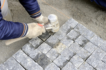 A worker places cobblestones patern on the street with rubber hammer manualy