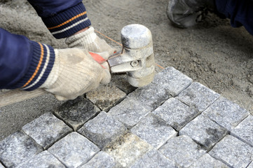 A worker places cobblestones patern on the street with rubber hammer manualy