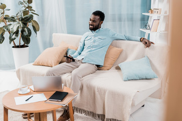 african american man watching TV and sitting on sofa in living room