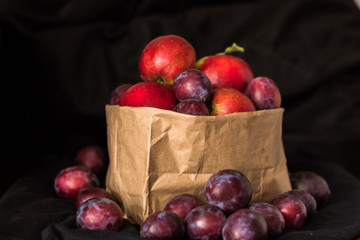 Plums and apples in the craft package on a black background.