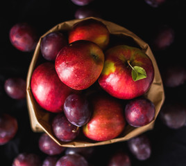 Plums and apples in the craft package on a black background.