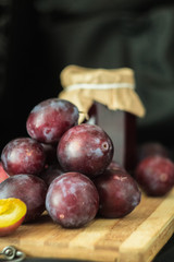 Fresh garden plums and jar of jam at the wooden board.