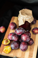 Fresh garden plums and jar of jam at the wooden board.