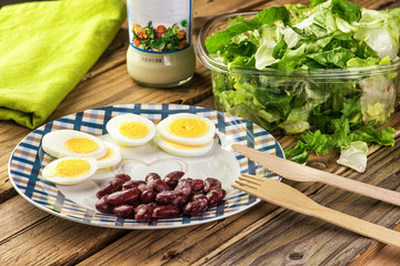 Vegetarian salad of green leaves with egg and beans on a wooden table.	