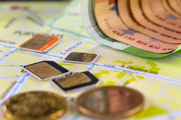 Close-up gsm cards of different sizes lie on the city map surrounded by coins and Euro banknotes.