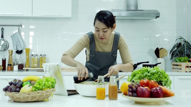 Asian man using tablet to assist him prepare healthy food at kitchen. Man try to cooking by himself at home. People with healthcare and technology concept.