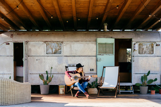Young woman playing guitar near caravan
