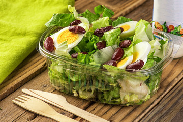 Vegetarian salad of green leaves with egg and beans on a wooden table.	