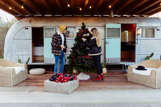 Young couple decorating Christmas tree near trailer