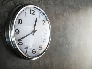 White steel round clock on grey concrete wall