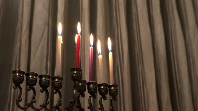 Six candles in hanukkiah are burning on light curtain background on the fifth day of the Jewish holiday Hanukkah. Hanukkiah rotates around its vertical axis. Selective focus. Slow motion. 4k